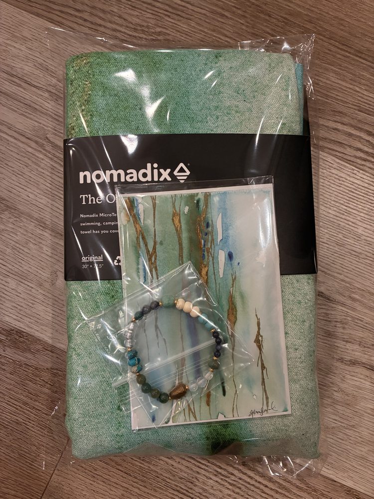 Nomadix Original Towel in its bag with the Illumination art card and a handmade bracelet